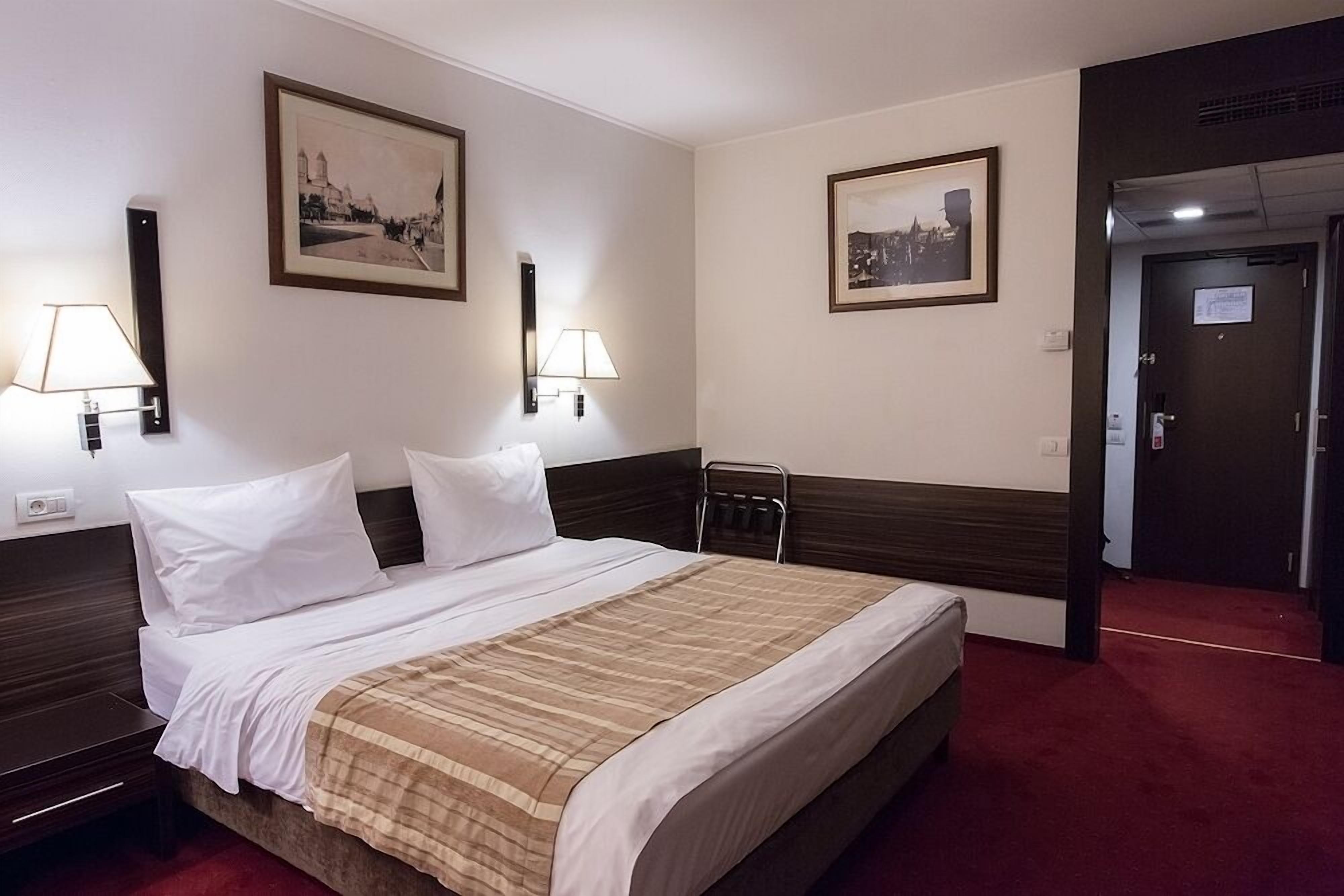Una habitación de hotel con una cama grande, dos lámparas de noche y dos cuadros en las paredes.