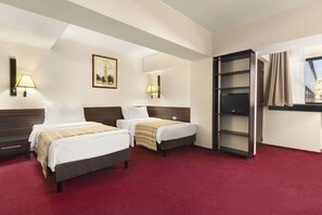 Ein Hotelzimmer mit zwei Betten, einem roten Teppich, einem hölzernen Kopfteil, einem Bücherregal und einem Fenster mit Vorhängen.
