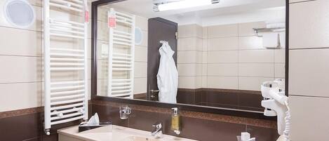 A hotel bathroom with a large mirror, a sink, a towel rack, and a hairdryer.