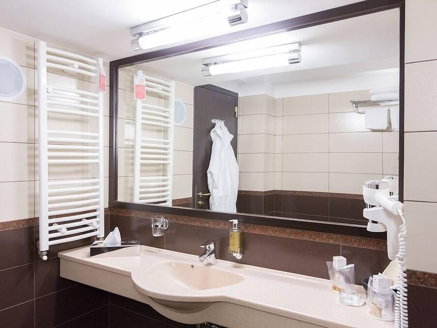 Een hotelbadkamer met een grote spiegel, een wastafel, een handdoekrek en een haardroger.