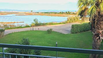 A view from a balcony overlooking a parking area with a body of water and distant hills.