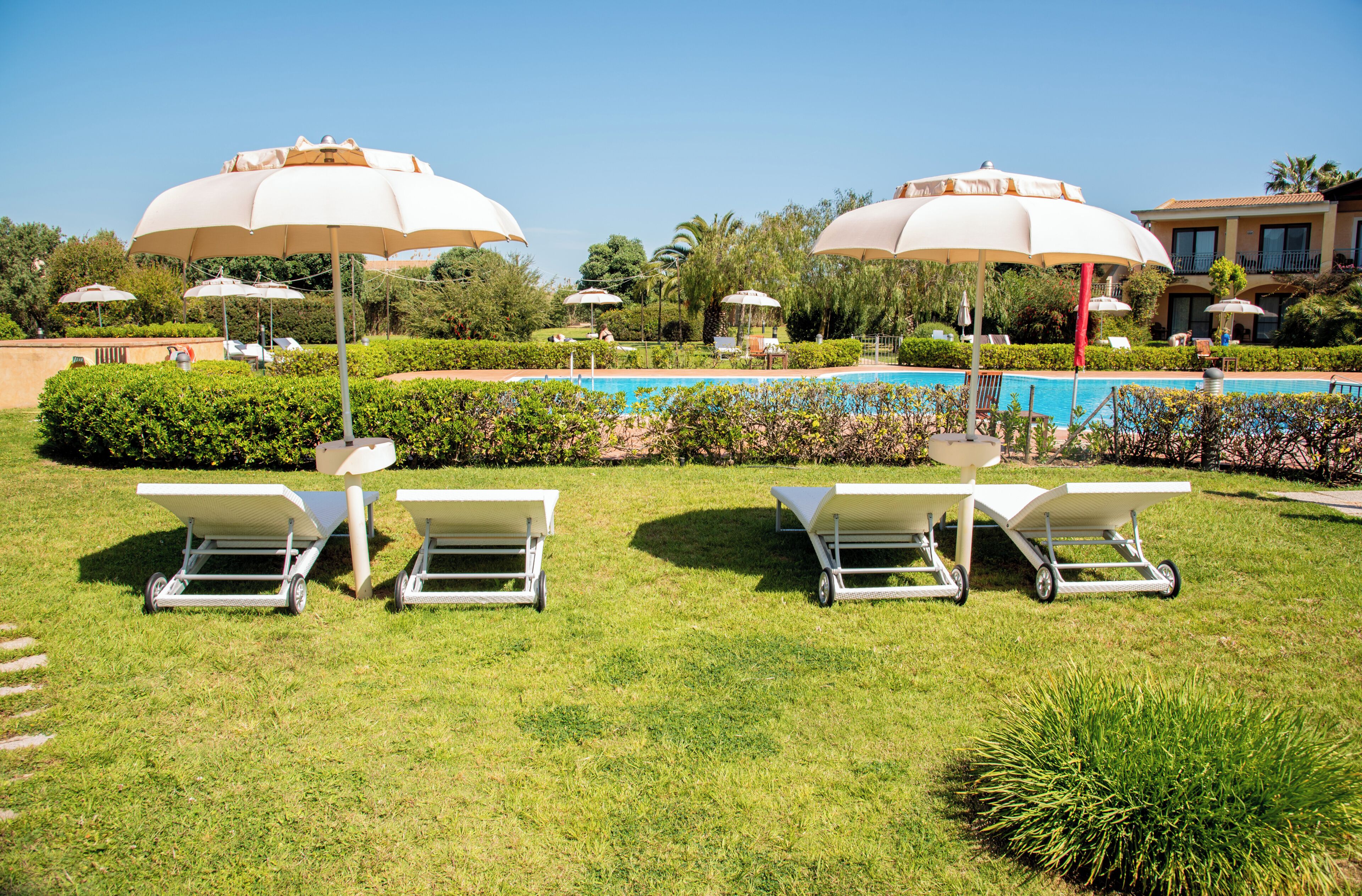Un espace aménagé au bord de la piscine, avec des chaises longues et des parasols, une piscine et une végétation bien entretenue.