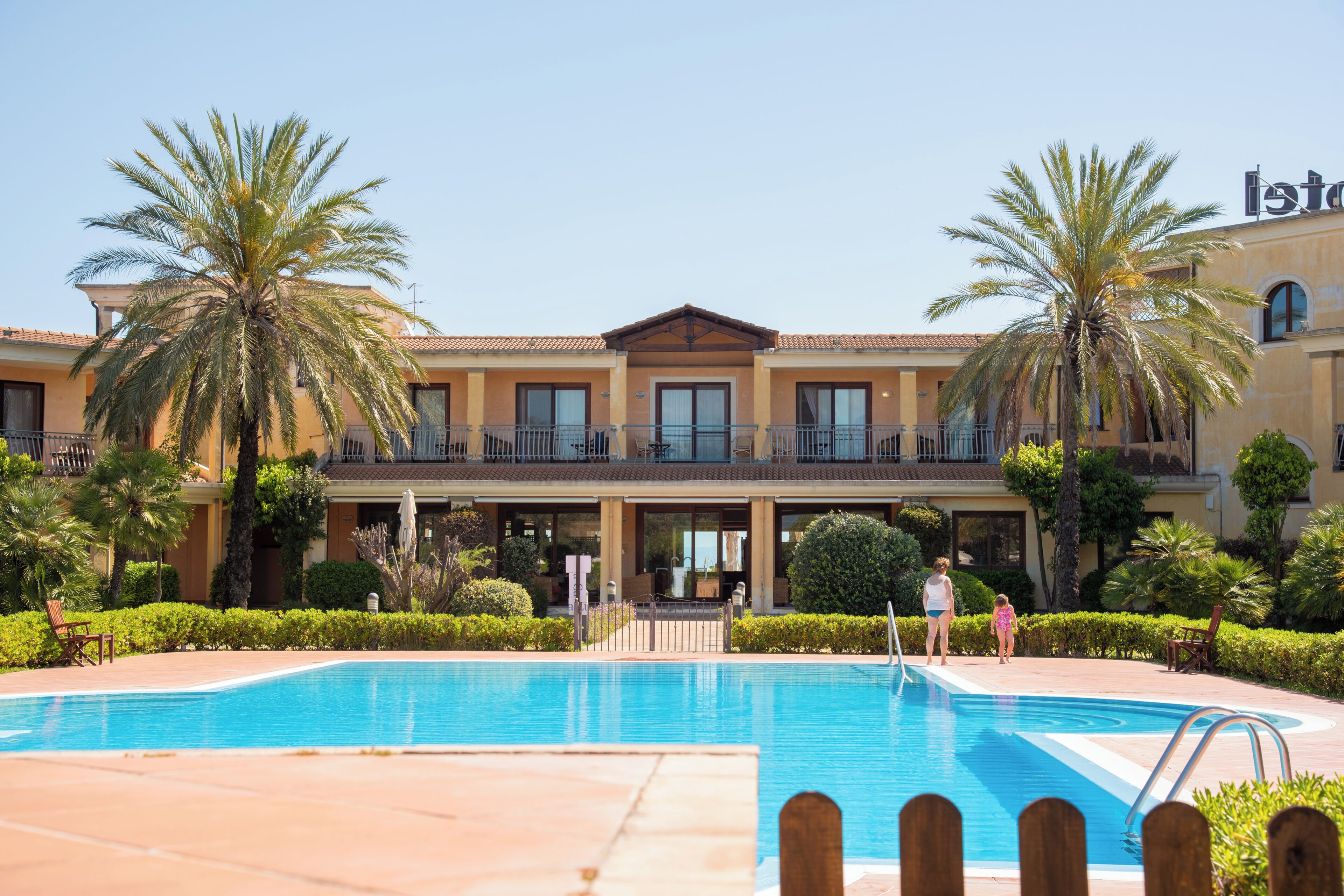 Un hotel amb piscina, palmeres i un cel blau clar.