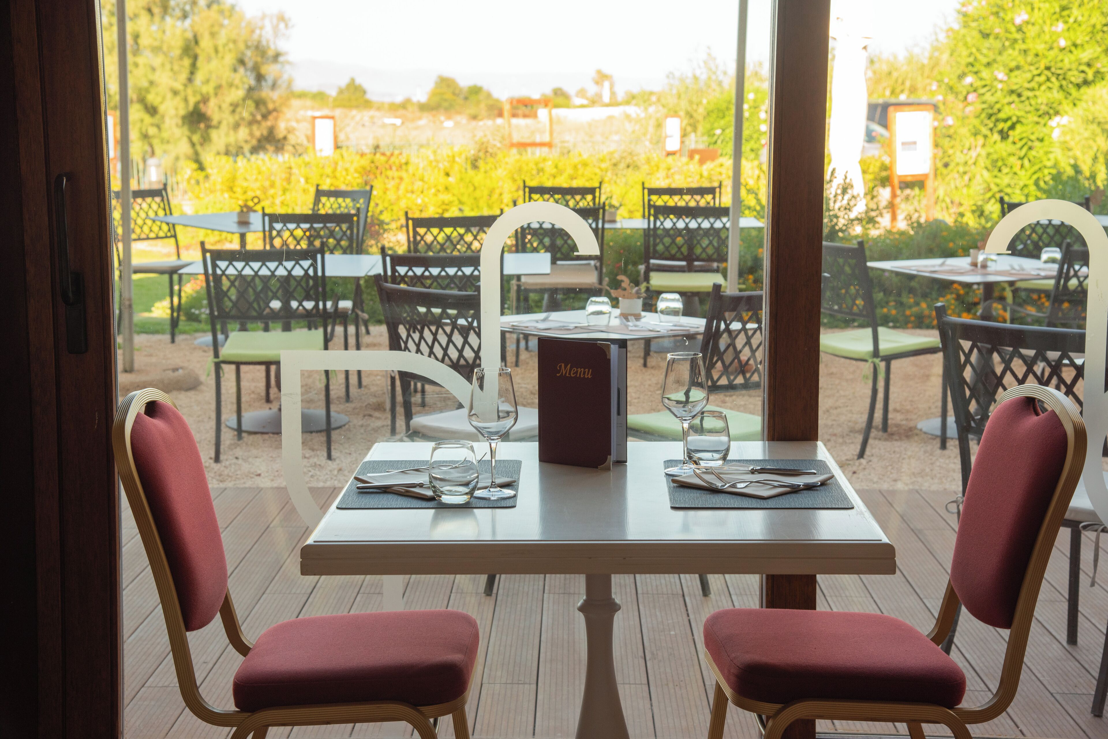 Area pranzo all'aperto con tavoli e sedie, un espositore per il menu e vista su un vigneto.