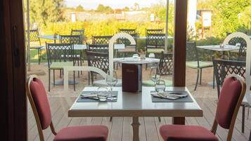 Area pranzo all'aperto con tavoli e sedie, un espositore per il menu e vista su un vigneto.