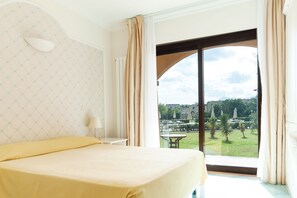 Una habitación de hotel con una cama, una mesita de noche, una lámpara y un ventanal con cortinas.