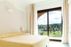 Una habitación de hotel con una cama, una mesita de noche, una lámpara y un ventanal con cortinas.