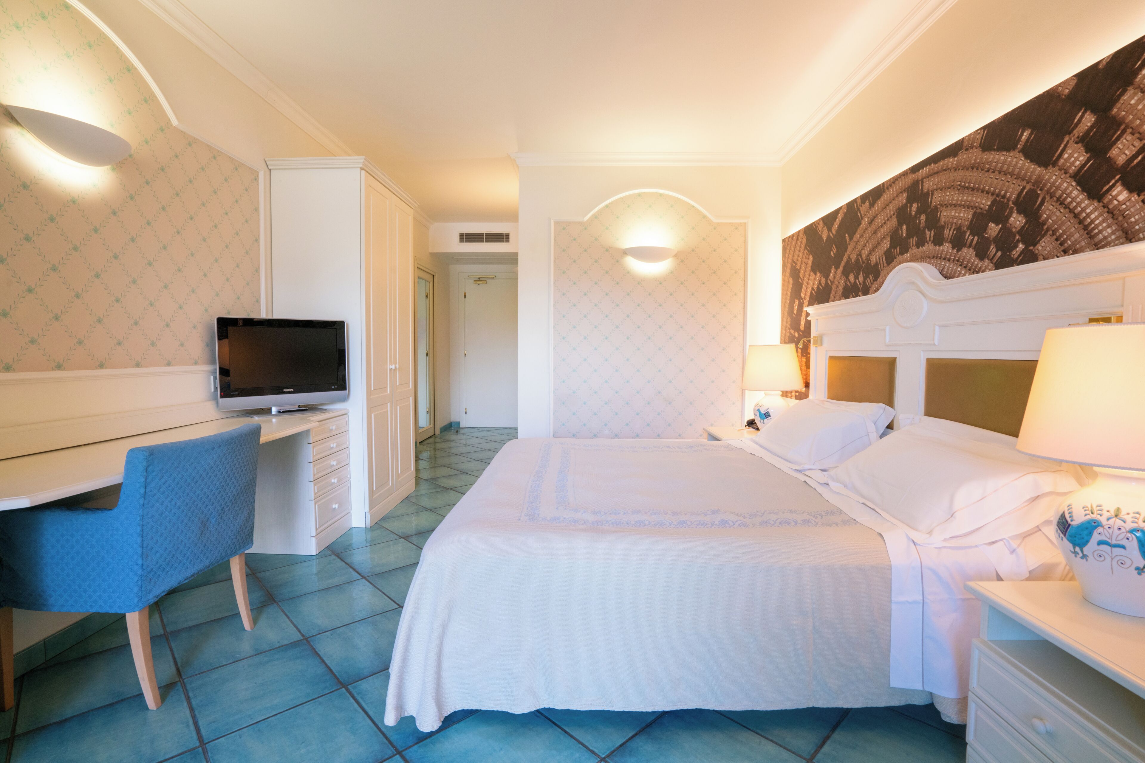 Een hotelkamer met een bed, bureau, televisie en een wand met een decoratief patroon.