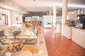 Zona de bufé con diferentes opciones de comida, una máquina de café y mesas y sillas.