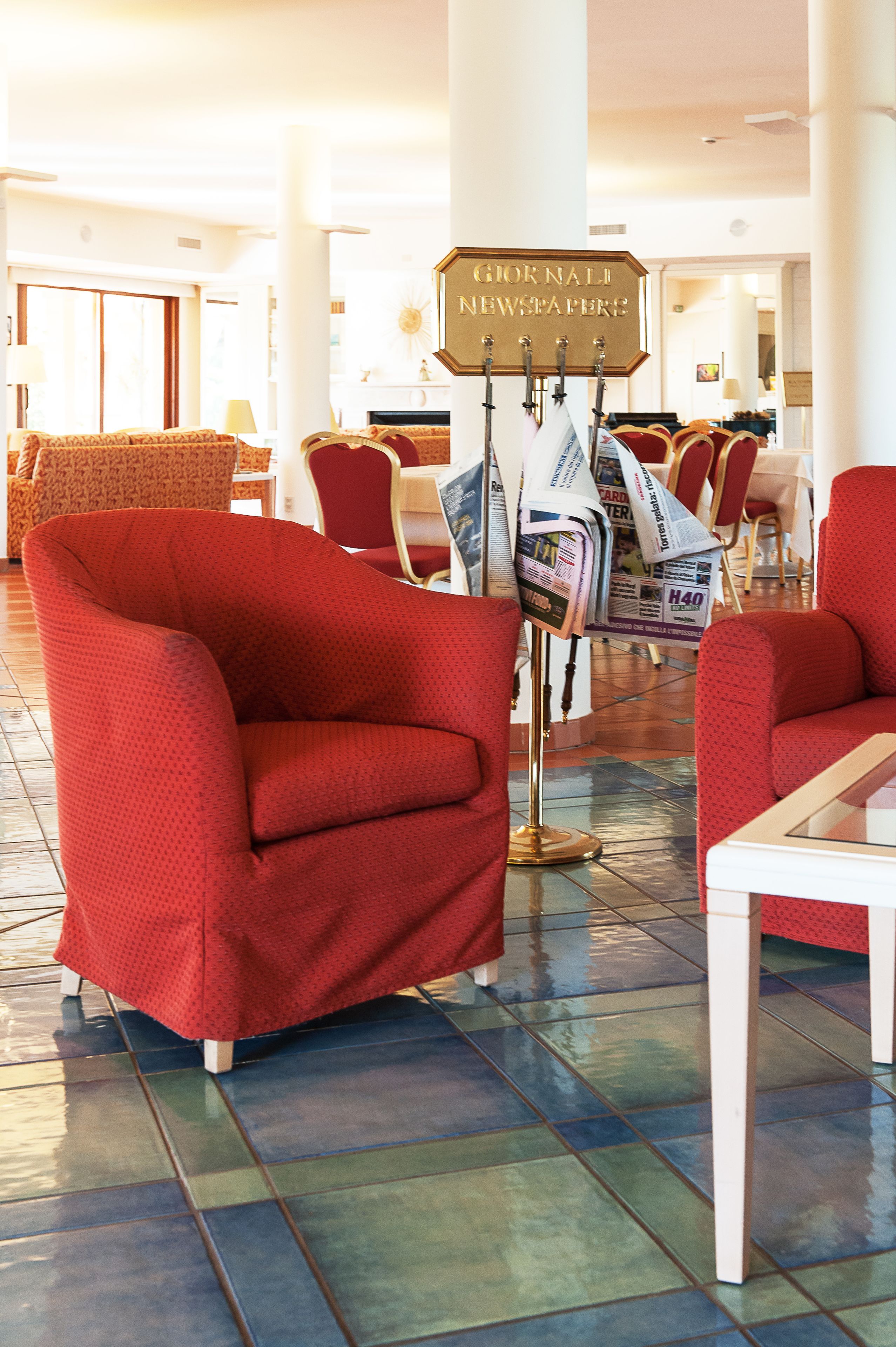 A lobby with red armchairs, a newspaper stand, and a tiled floor.