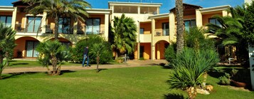 Un hotel con varios balcones, palmeras y un césped bien cuidado.