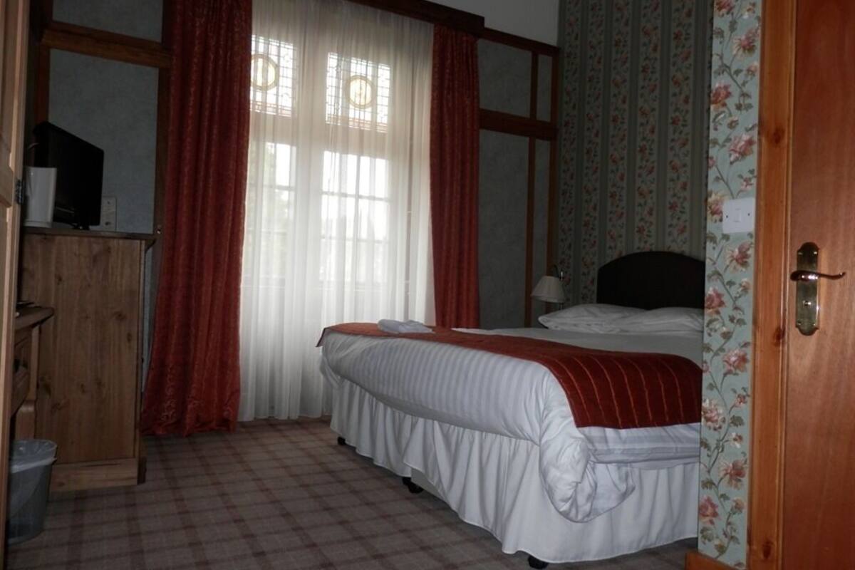 Um quarto com cama, guarda-roupa de madeira, escrivaninha com computador e janela com cortinas.
