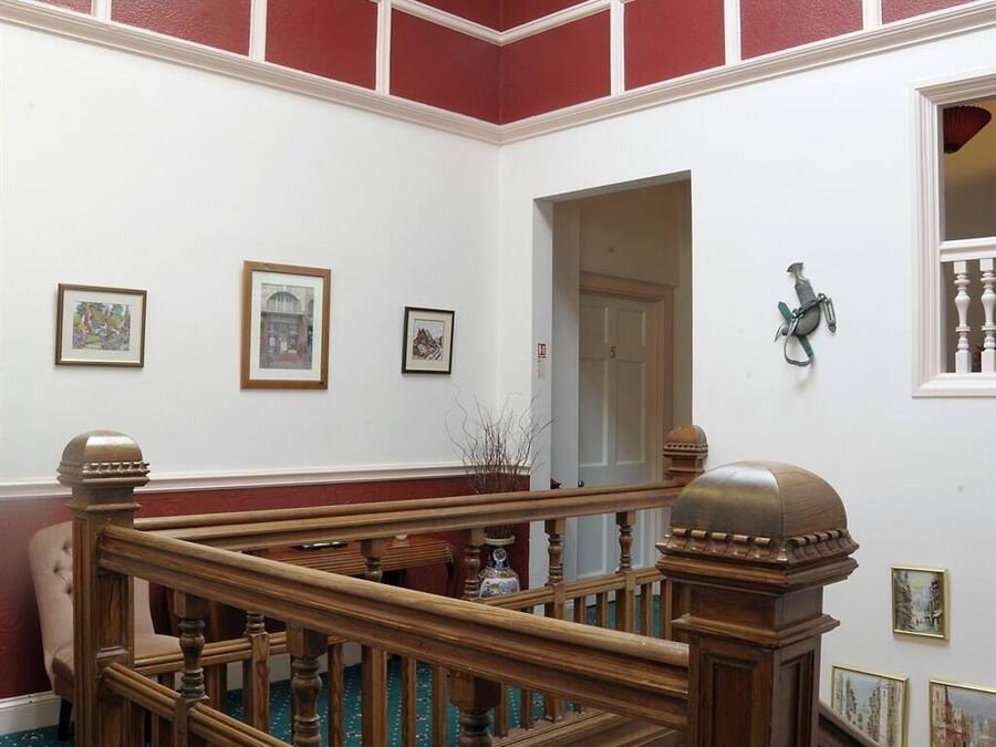 A staircase with wooden balusters and a handrail, leading to a landing with framed artwork on the walls.