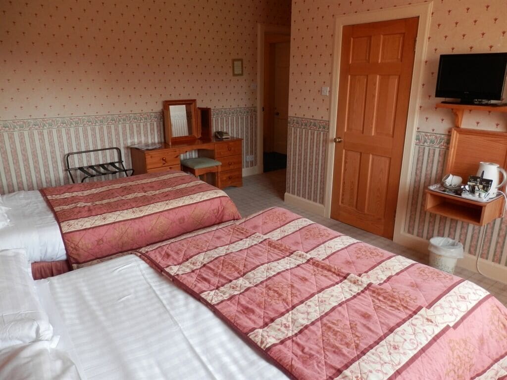 Un dormitorio con dos camas, un aparador de madera, un televisor y una mesita con un hervidor.