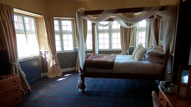 A four-poster bed with a canopy, a wooden dresser, and a patterned carpet in a room with large windows and curtains. - The Glen Guesthouse (Selkirk)