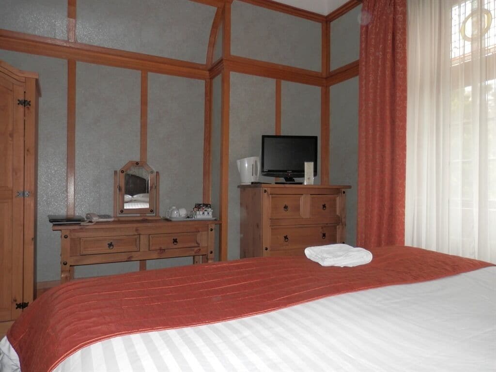 Ein Schlafzimmer mit Bett, Holzkommode, Fernseher und Spiegel.