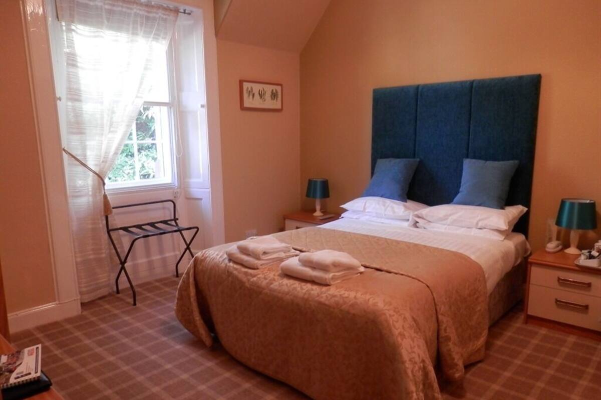 Quarto com uma cama, duas mesas de cabeceira, uma janela com cortinas e um quadro pendurado na parede.