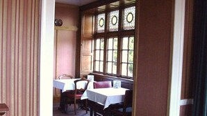 A dining area with tables and chairs, a window with decorative glass panes, and a door leading to another room. - The Glen Guesthouse (Selkirk)