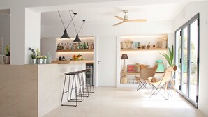 A modern kitchen with a bar area, bar stools, and a ceiling fan. - Aparthotel Niu d´Aus (Santanyi)