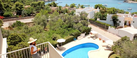 A residential area with a swimming pool, a balcony with a railing, and a view of the sea with boats.
