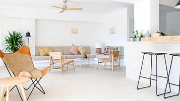 Una sala de estar moderna con un sofá, dos sillones, una mesa de centro y una zona de bar con taburetes.