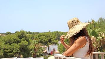 A balcony with white railings overlooking a lush green landscape with trees and a clear blue sky.