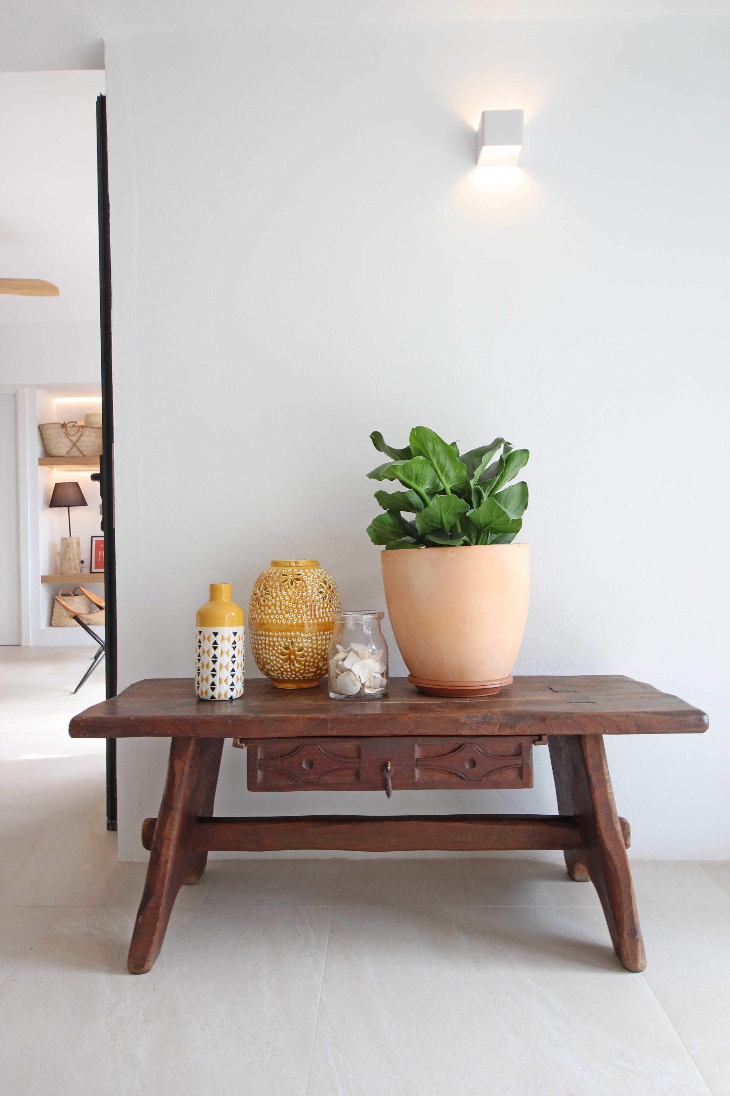 Une table en bois, sur laquelle se trouvent un pot de fleurs, un vase jaune et un bocal en verre.
