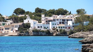 A coastal town with white buildings, clear blue water, and rocky terrain. - Aparthotel Niu d´Aus (Santanyi)