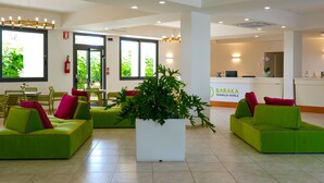 Un vestíbulo de hotel con sofás verdes, una planta grande en maceta y un mostrador de recepción.