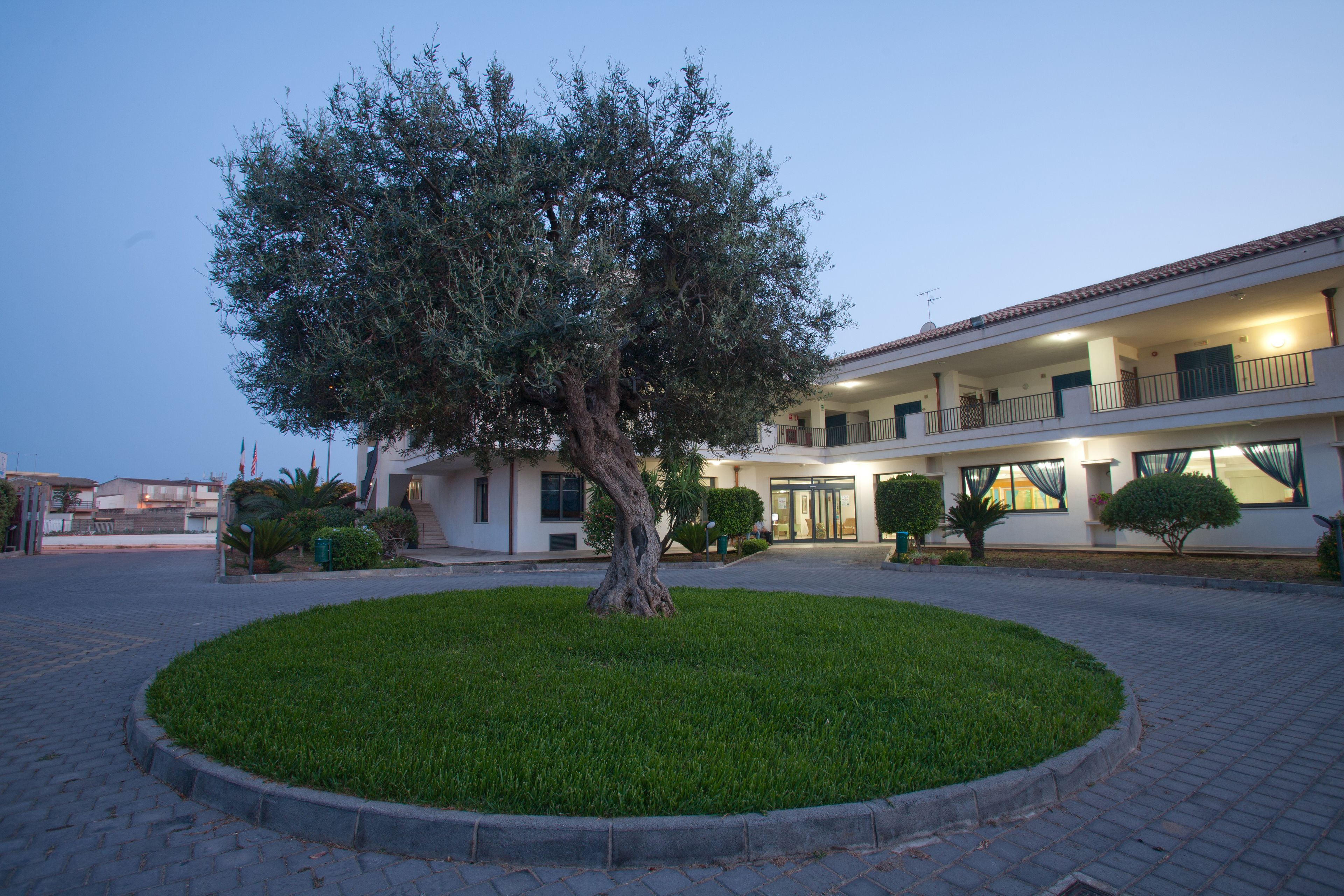 A building with a central lawn and a tree, featuring a double-story structure with balconies and a well-lit entrance.
