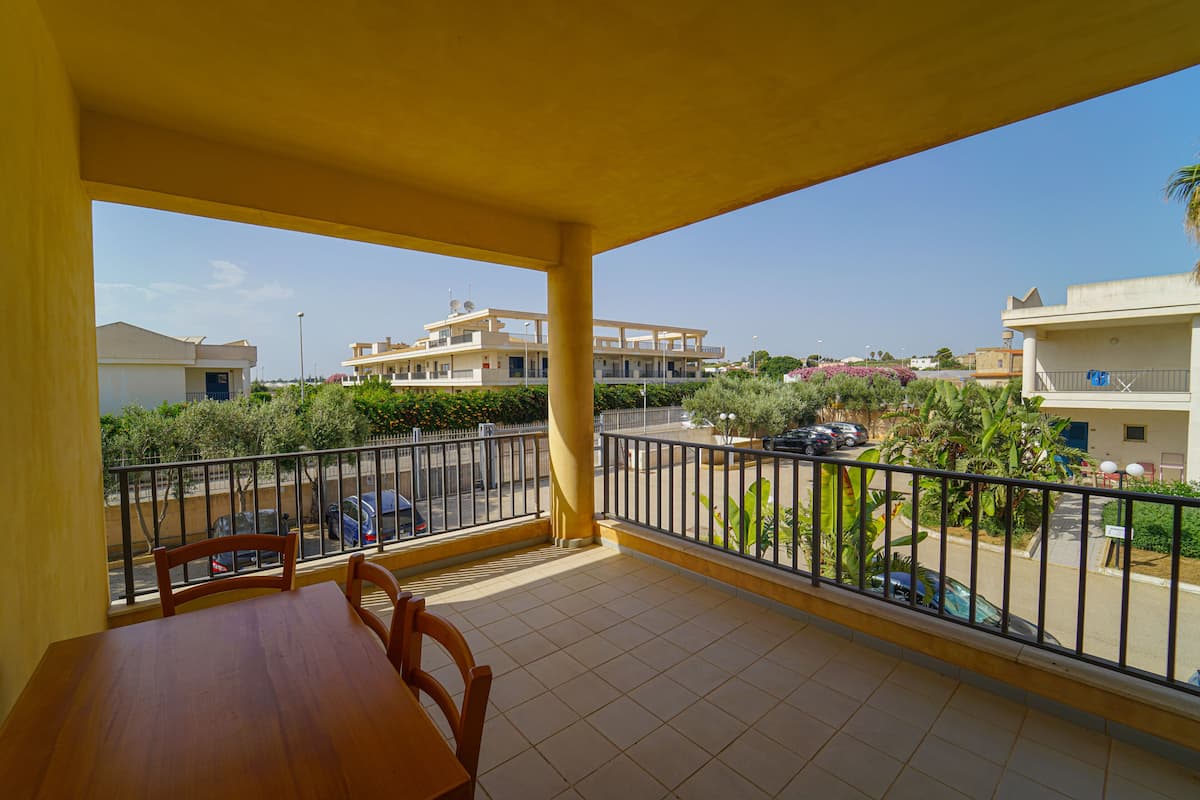 A balcony with a wooden table and chairs, a view of a residential area, and a clear sky.