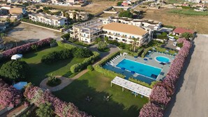 Vista aérea de un complejo turístico con piscina, una zona de estar cubierta al aire libre y vistas del pueblo y el mar circundantes.
