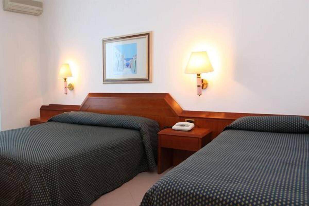 Ein Hotelzimmer mit zwei Einzelbetten, einem Holz-Kopfteil, Nachttischlampen, einem gerahmten Bild an der Wand und einem Telefon auf dem Nachttisch.