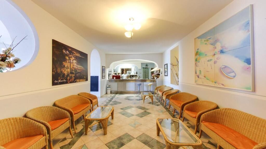 Una hall d'albergo con divani in vimini, un tavolino da caffè in vetro e un'area bar sullo sfondo.
