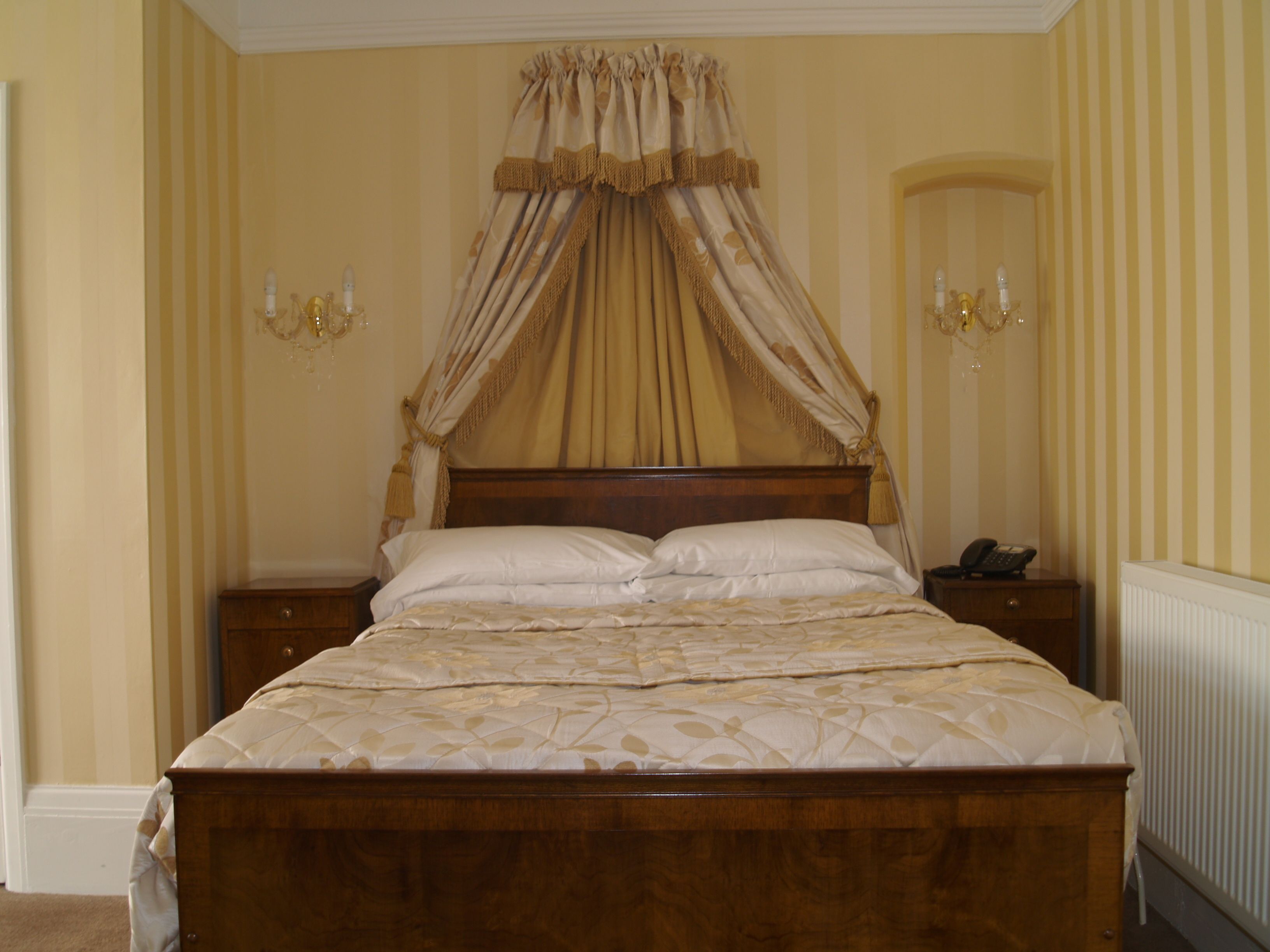 Ein Schlafzimmer mit einem hölzernen Bett, einem Baldachin, zwei Nachttischen und einem Beistelltisch.