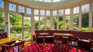 A conservatory with a red patterned floor, a wooden table, and a leather sofa. - The Normanhurst Hotel (Sale)