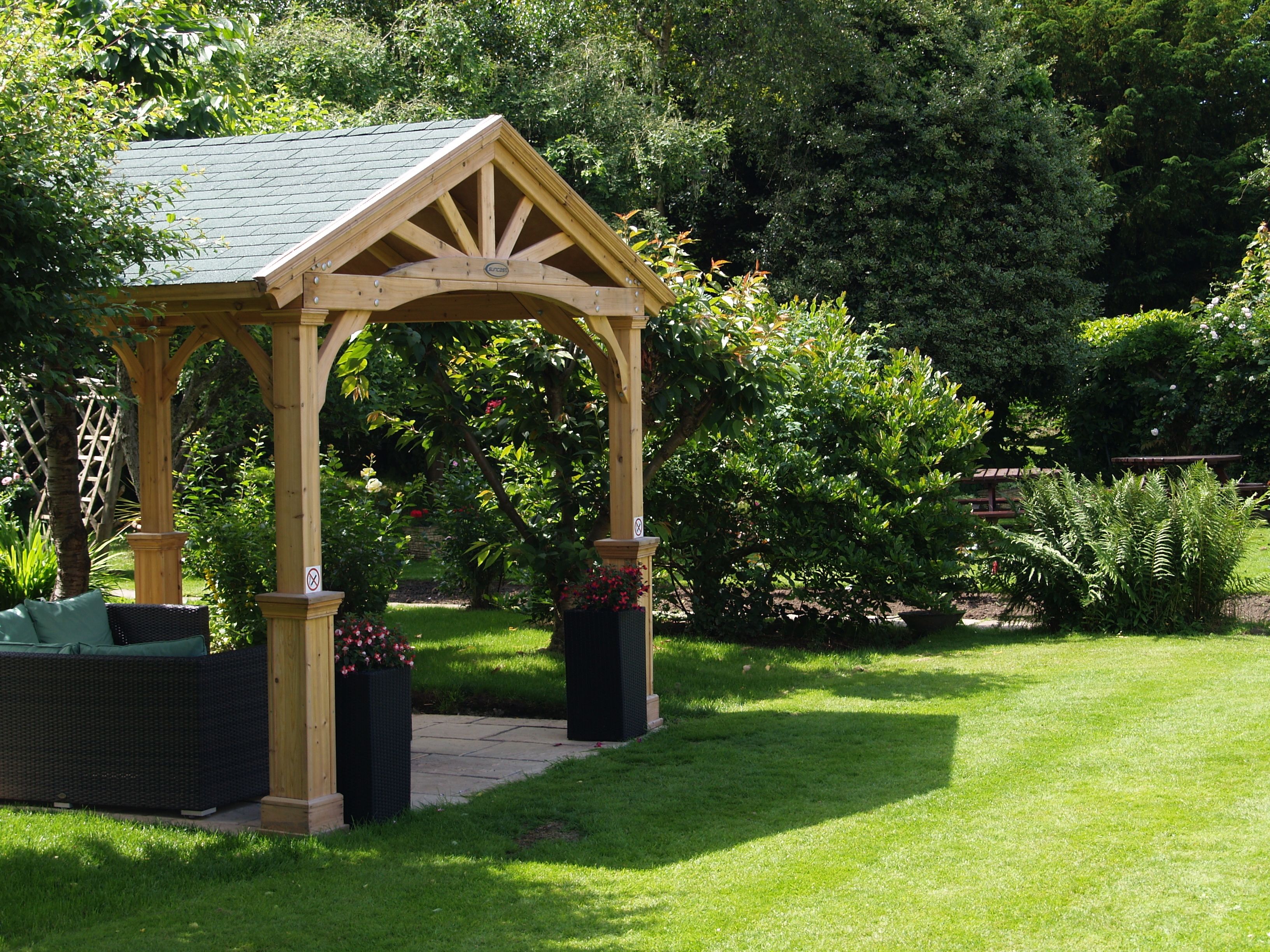 A wooden gazebo with a tiled roof in a lush garden setting.