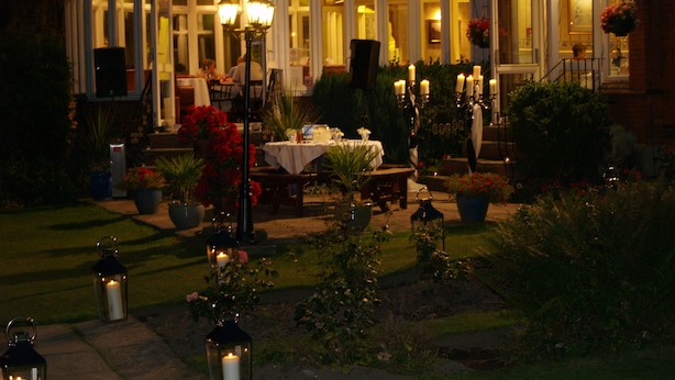A conservatory with a glass roof, surrounded by a garden with potted plants and candles. - The Normanhurst Hotel (Sale)