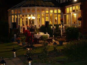 A conservatory with a glass roof, surrounded by a garden with potted plants and candles. - The Normanhurst Hotel (Sale)