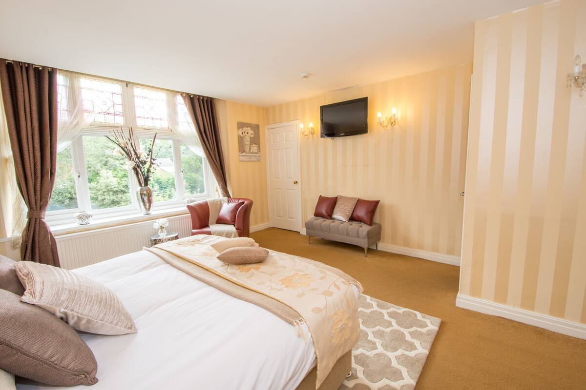 A hotel room with a large bed, a sofa, a TV, and a window with curtains.