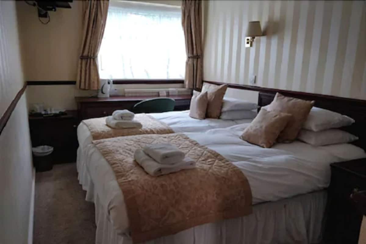 A hotel room with two beds, a desk, a chair, and a window with curtains.