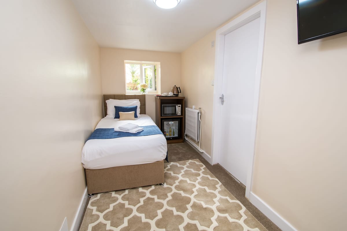 A bedroom with a bed, a window, a radiator, and a television on the wall.