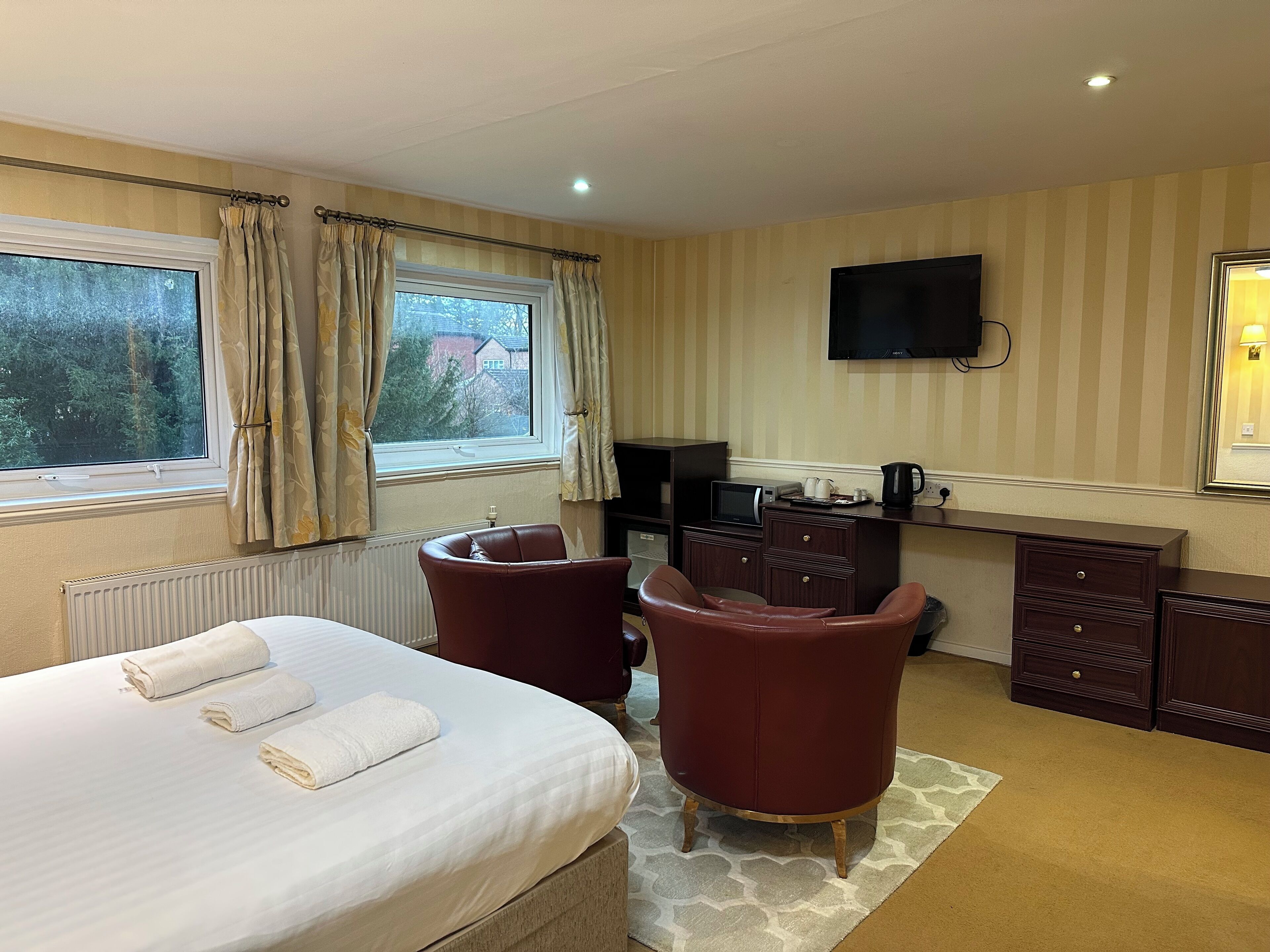 Habitación de hotel con cama, dos sillones, escritorio con computadora, televisor y ventana con cortinas.