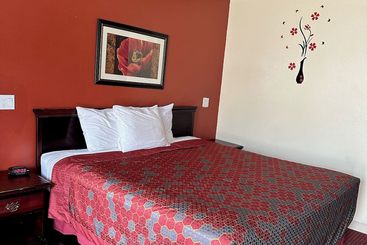 Une chambre d’hôtel avec un grand lit, une table de chevet, un tableau encadré au mur et un motif floral décoratif sur le mur.