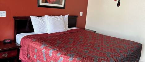 A hotel room with a large bed, a nightstand, a framed picture on the wall, and a wall decal of flowers.