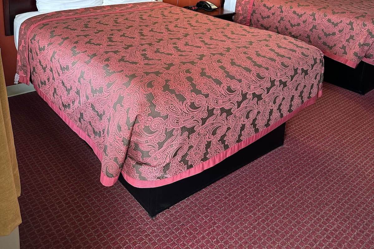 Une chambre d’hôtel avec deux lits, chacun recouvert d’une couvre-lit à motifs, agrémenté d’oreillers blancs et orné d’une œuvre d’art florale encadrée au mur.