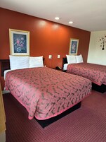 Habitación de hotel con dos camas, cada una con colcha estampada, almohadas blancas y una obra de arte floral enmarcada en la pared.