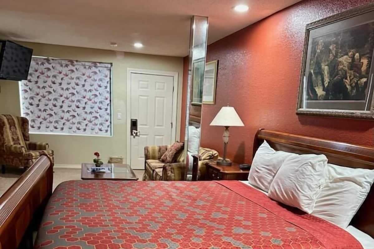 Une chambre d’hôtel avec un grand lit, une table de chevet, une lampe, une chaise, un bureau et une fenêtre avec des rideaux.