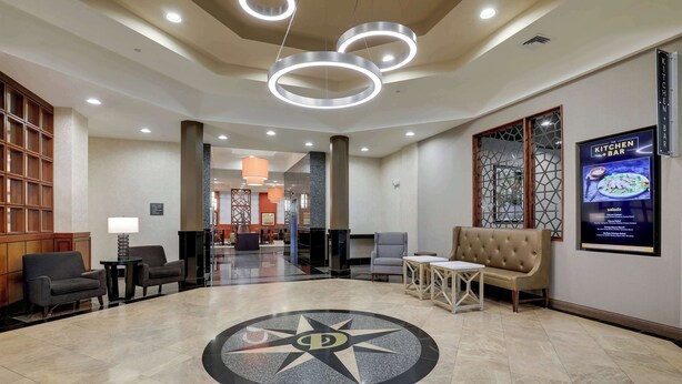 A hotel lobby with a central circular floor design, seating areas, and a Kitchen+Bar sign. - Drury Inn & Suites Charlotte Northlake (Charlotte)