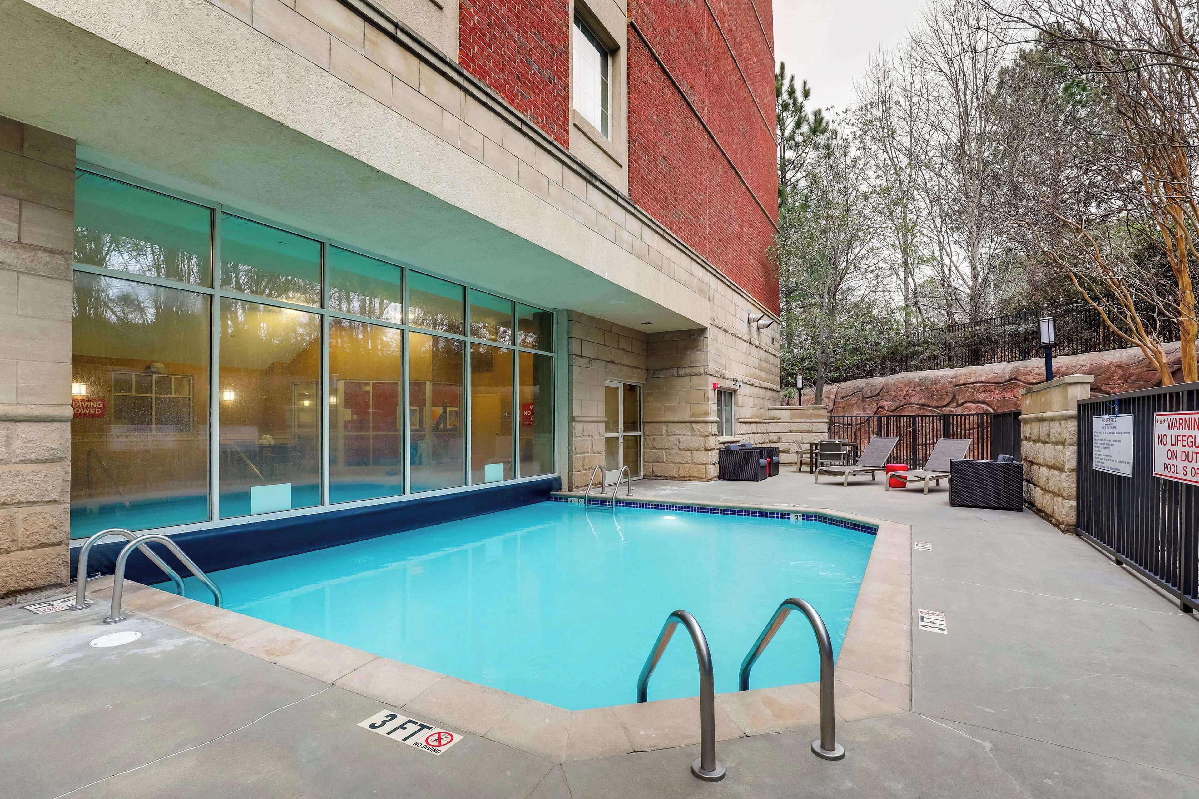 Una piscina con pared de piedra y ventanas de cristal, una silla de salvavidas y un cartel de advertencia.